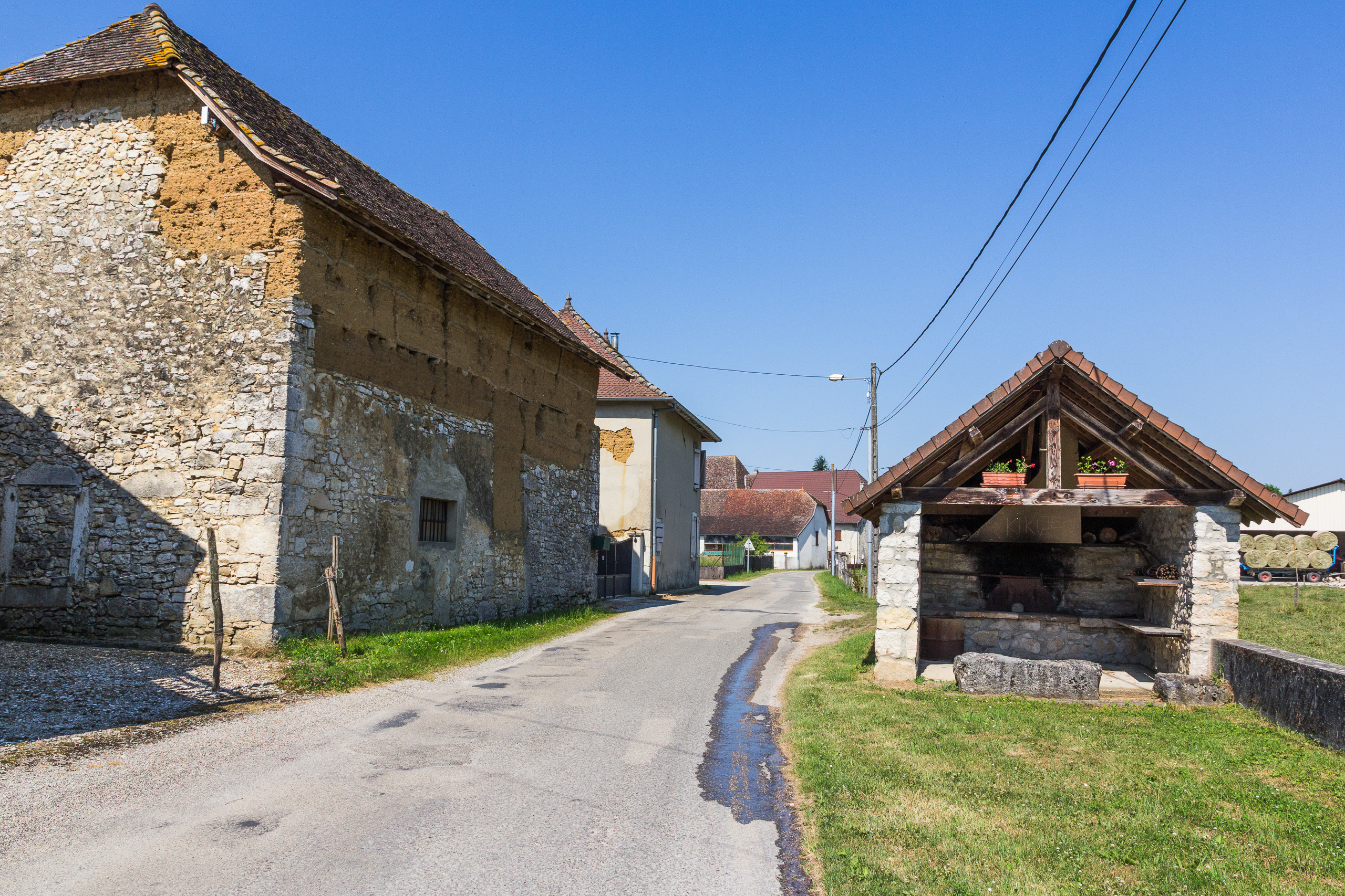 Dorfstraße mit altem Waschhaus (Lavoir) und Geranien